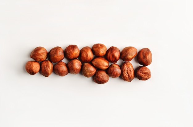 A horizontal row of dry raw hazelnuts on a studio white background. Food composition top of the view.