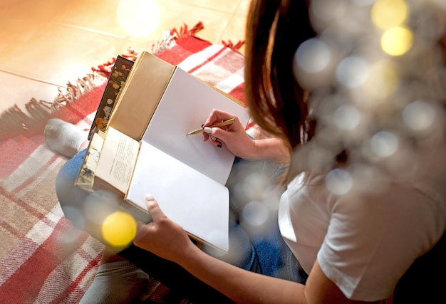 Horizontal shot of a happy woman sitting on the floor in the kitchen with an open notepad waiting for a delicious pie baking in the oven