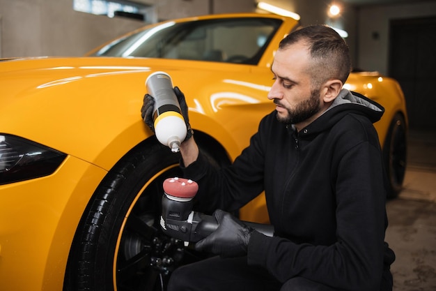 Horizontal shot of man auto service worker wearing black clothes putting special polish wax