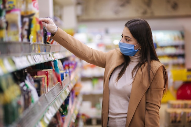 Horizontal shot of woman in protective mask and gloves reading label with price at goods while