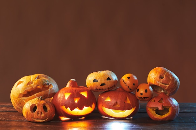 Horizontal studio shot of Halloween still life composition made of carved pumpkins and tangerines on brown surface, copy space