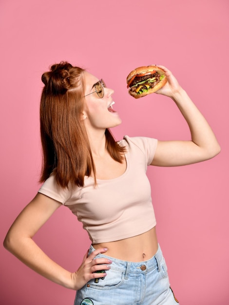 Horizontal studio shot of pretty young woman holding a burger and a glass of soda