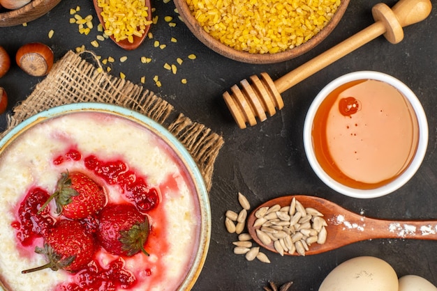 Horizontal view of delicious breakfast served with strawberries jam in a bowl and spikes hazelnuts eggs rice honey on dark color background