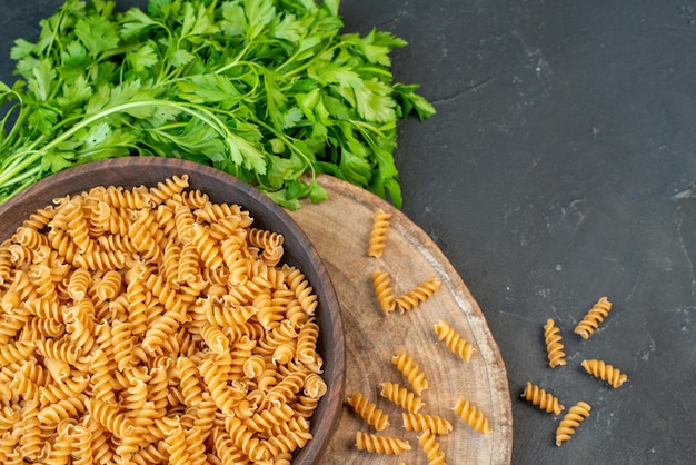 Horizontal view of raw pastas inside and outside brown pot green on the right side on dark blue color background