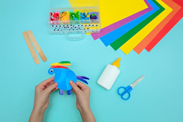 Horse made of paper on a blue table, children's hands make crafts of the magic color of the horse