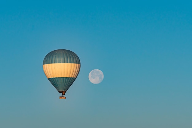 Hot-air balloon flying over the Cappadocia region in Turkey in a blue sky with a full moon