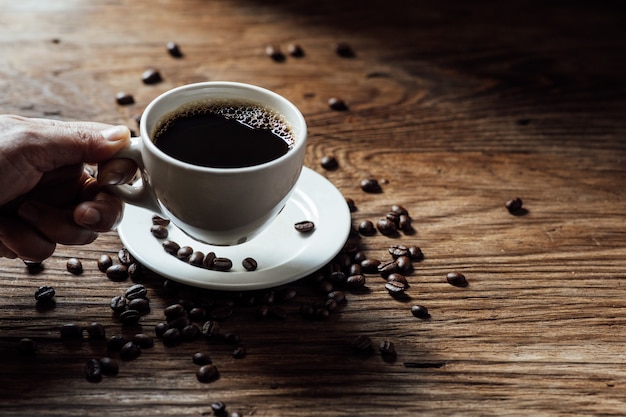 Hot black coffee cup and coffee beans on wooden table with natural light in the morning