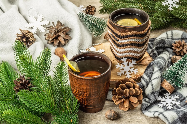 Hot black tea and lemon with winter decor. Cozy sweater, fir tree branches, nuts, snowflakes. Festive seasonal arrangement, good mood concept, rustic style