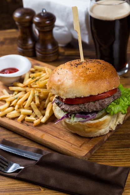 Hot burger serving on wooden board with dark beer