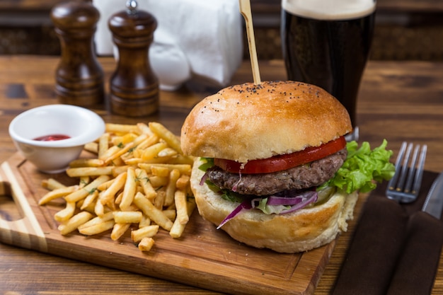 Hot burger on wooden board with dark beer