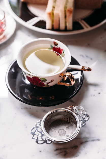 Hot Chamomile Tea served in porcelain vintage cup with stainless steel tea strainer infuser.