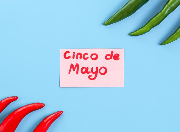 Hot chilli peppers of green and red color lie on the sides with a pink sheet cinco de mayo