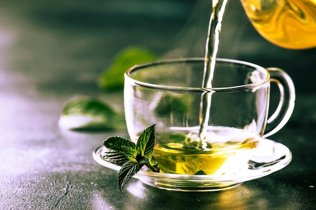 Hot chinese green tea with mint with splash pouring from the kettle into the cup steam rises dark background selective focus