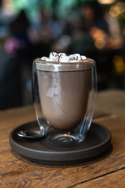 Hot chocolate or cocoa drink with marshmallow in glass cup on wooden table in cafe