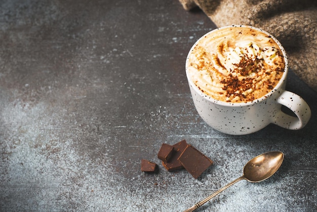 Hot chocolate or cup of coffe with foam and with a piece of chocolate on dark background