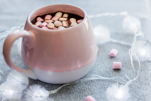 Hot chocolate  pink ceramic mug marshmallows and garland  gray knitted background