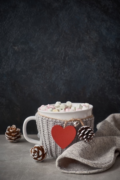 Hot chocolate with marshmallows, red heart on the cup on the table with pine cones, copy-space