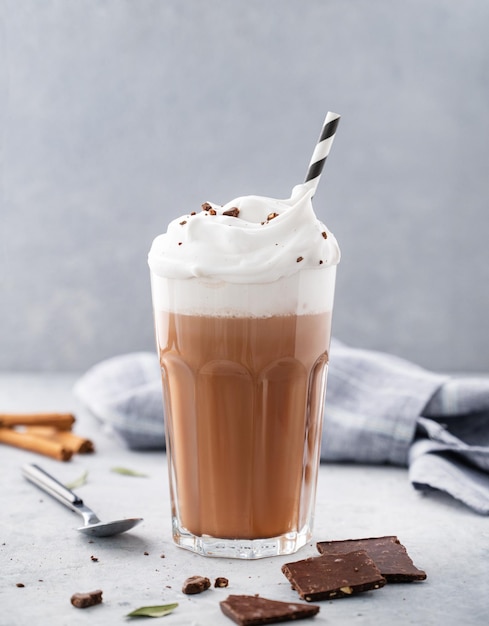 Hot chocolate with whipped cream and cinnamon in a tall glass on a blue background Front view and copy space