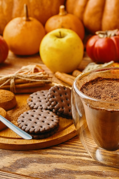 Hot cocoa cookies and autumn harvest on wooden table ripe pumpkins apples fall leaves and persimmons...