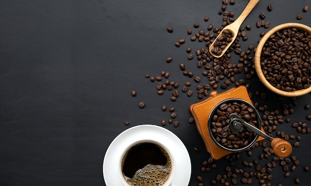 Hot coffee, bean and hand grinder on black table background. space for text. top view