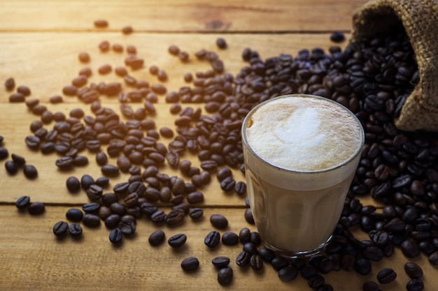 Hot coffee cappuccino and coffee bean on older wood table at morning time. Coffee break time.