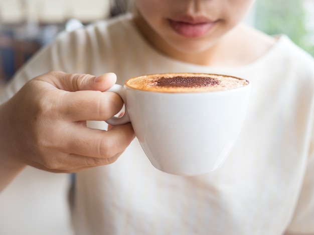 Hot coffee of cappuccino latte on white cup in hand ready to drink and blur background