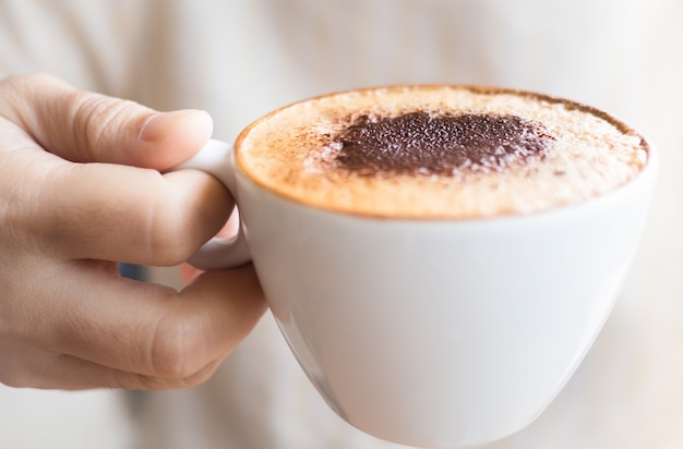 Hot coffee of cappuccino latte on white cup in hand ready to drink