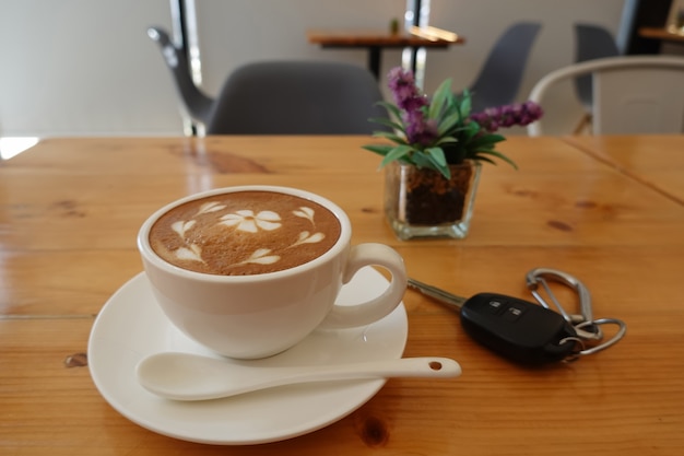 Hot coffee, cappuccino in a white coffee cup on a pine wood table And there is a car key next to it