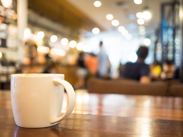 Hot coffee cappuccino in white cup on wooden table and blurred background cafe stores.