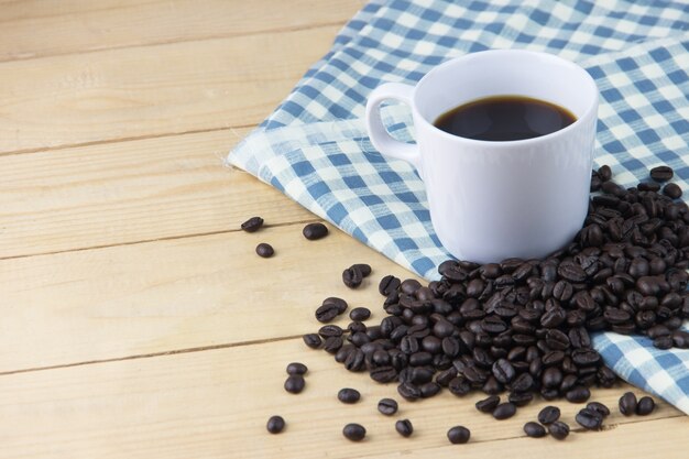 Hot coffee and coffee bean and blue and white napkin on wooden table