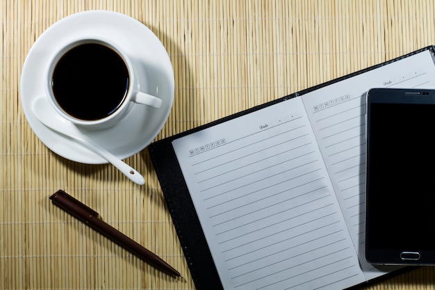 Hot coffee cup with notebook and mobile on the desk businessman