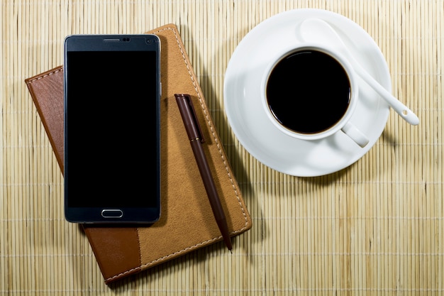 Hot coffee cup with notebook and mobile on the desk businessman