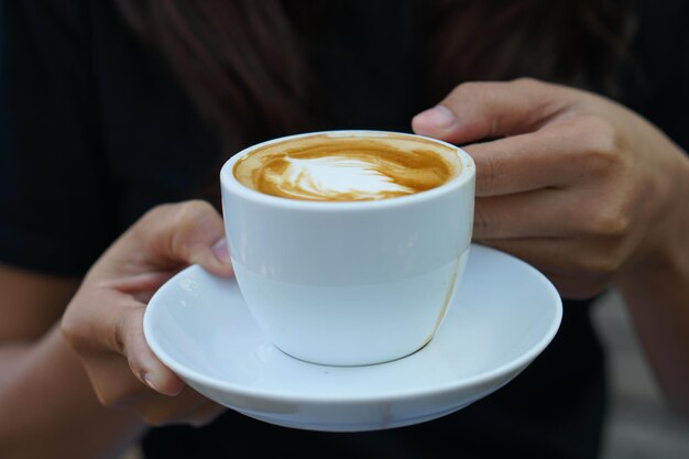 Hot coffee in human hands Coffee foam flowers in a white cup gray wood background