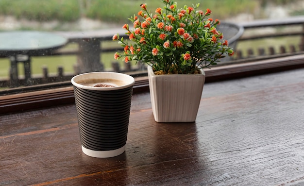 Hot coffee is placed on a wooden table with a flowerpot near the window.