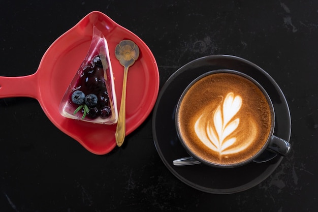 Hot coffee latte with latte art milk foam in cup and Blueberry Cake on black wood desk on top view As breakfast In a coffee shop at the cafeduring business work concept