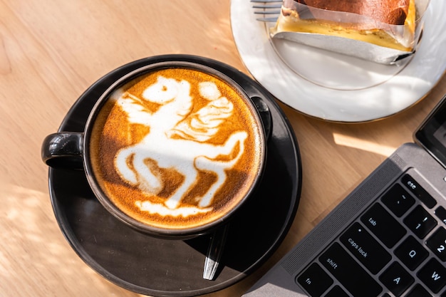 Hot coffee latte with latte art milk foam in cup mug and Homemade chocolate cake and laptop computer on wood desk on top view As breakfast In a coffee shop at the cafeduring business work concept