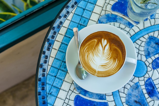 Hot coffee latte with latte art milk foam in cup mug on marble floor desk As breakfast In a coffee shop at the cafe during business work concept