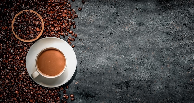 Hot coffee in a white coffee cup and many coffee beans placed around a on dark background.