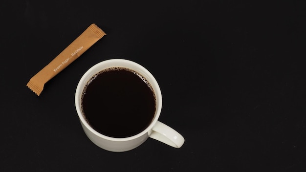 Hot coffee in white mug and brown sugar sachet in black background