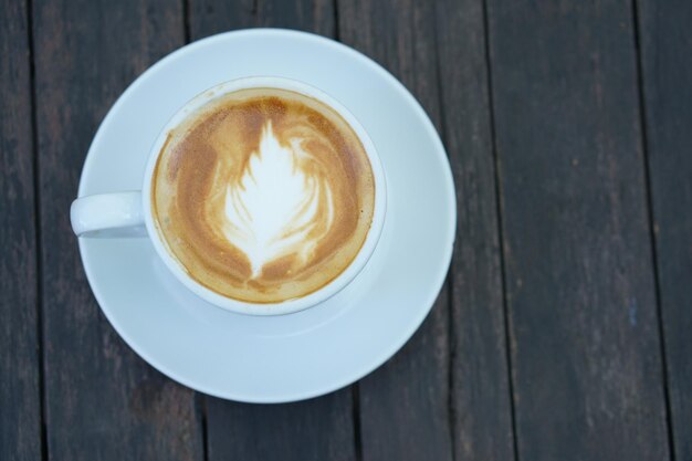 Hot coffee with floral foam in a white cup gray wood background