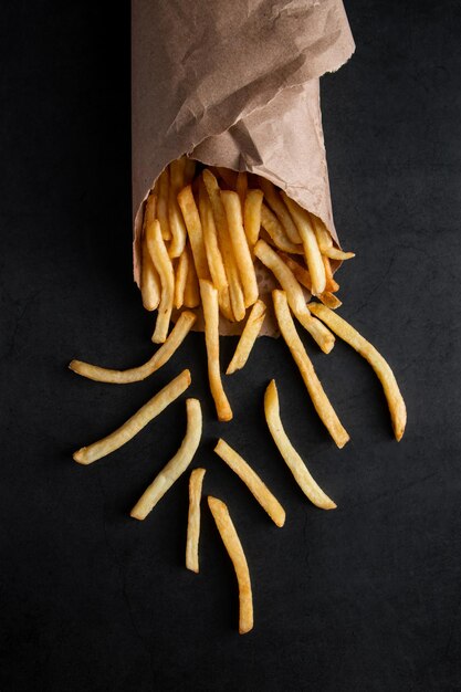 Hot crispy fries in a paper bag on a black background Tasty american fast food