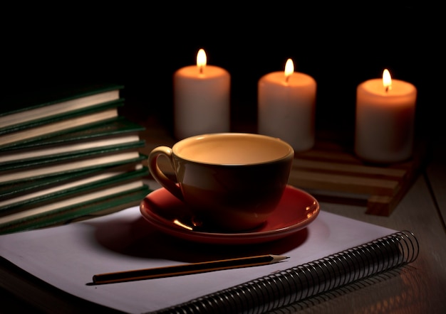 Photo hot cup of coffee with yellow smoke books notebook pencil and burning candles desk table