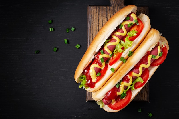 Hot dog with grilled sausage tomato and lettuce on dark background American hotdog Top view overhead