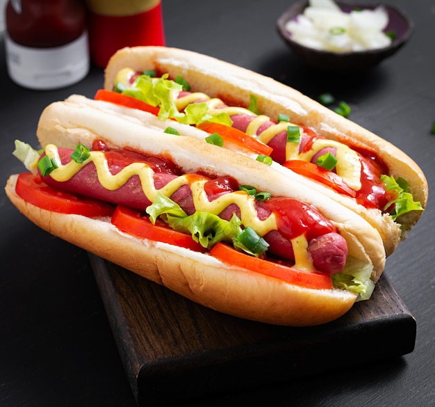 Hot dog with grilled sausage tomato and lettuce on dark background American hotdog