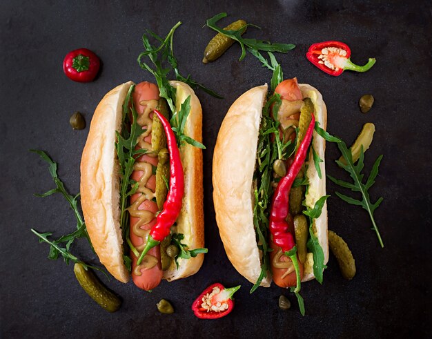 Hot dog with pickles, capers and arugula on black background.