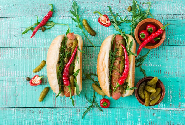 Hot dog with pickles, capers and arugula on wooden table. 