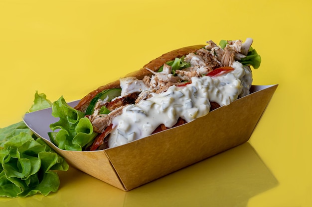 Hot dog with sausage in a paper box with tomatoes and corn chili peppers cucumber and lettuce On a red background Fast food