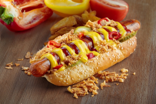 Hot dog with yellow mustard and ketchup on wooden board