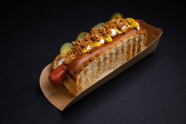 Hot dogs in paper plates with sausages and sauce on a black background