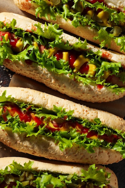 Hot dogs with pickles and lettuce leaves on dark gray background top view